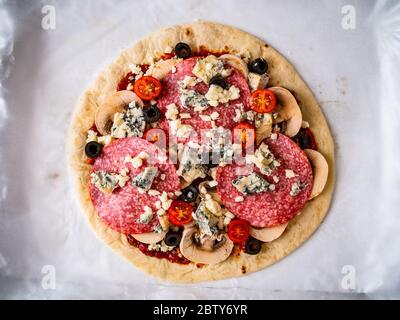 Ungebackene Pizza mit Salami, Champignon, Oliven und Kirschtomaten Stockfoto