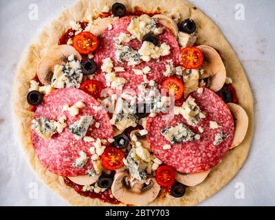 Ungebackene Pizza mit Salami, Champignon, Oliven und Kirschtomaten Stockfoto