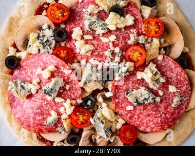 Ungebackene Pizza mit Salami, Champignon, Oliven und Kirschtomaten Stockfoto