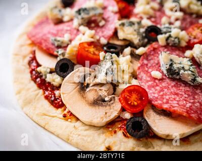 Ungebackene Pizza mit Salami, Champignon, Oliven und Kirschtomaten Stockfoto