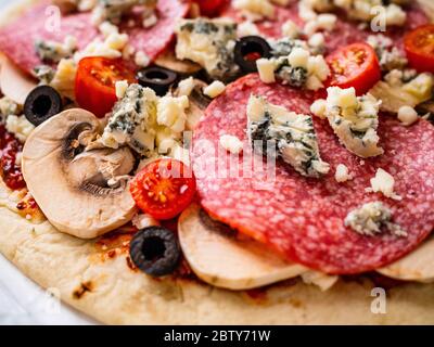 Ungebackene Pizza mit Salami, Champignon, Oliven und Kirschtomaten Stockfoto