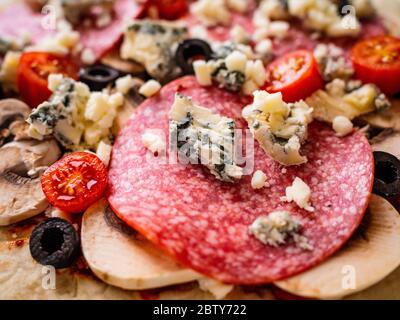 Ungebackene Pizza mit Salami, Champignon, Oliven und Kirschtomaten Stockfoto