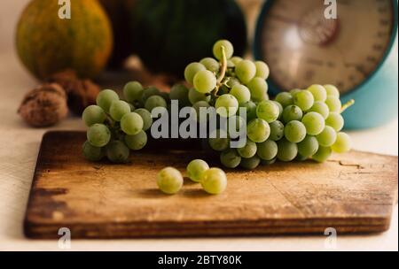 Herbst noch leben. grüne Trauben liegen auf Holzbrett. Im Hintergrund sind Kürbisse, Walnüsse und Skalen. Herbst Ernte Konzept. Happy Thanksgiving Stockfoto