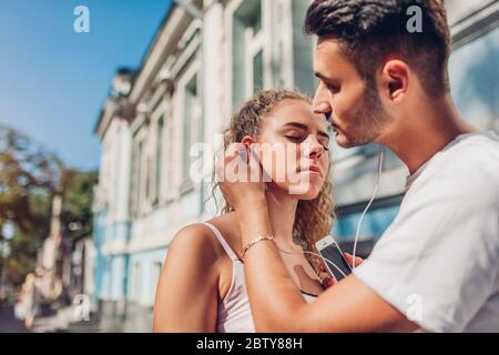 Gemischtes Rennpaar in der Liebe, die Musik in der Stadt zu hören. Arabischer Mann legt Ohrhörer in das Ohr der Freundin auf der Straße Stockfoto