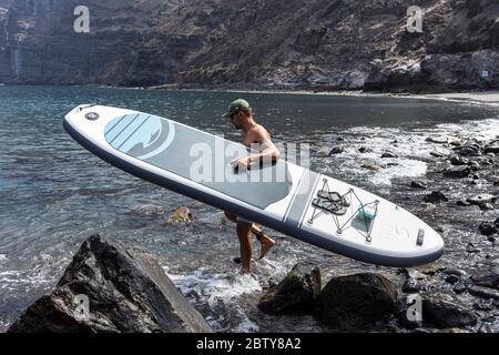 Playa de los Guios, Los Gigantes, Santiago del Teide, Teneriffa, Kanarische Inseln, Spanien. 28 Mai 2020. Zwei junge Männer gehen auf SUP, stehen Paddle Boards vom Strand während Phase zwei Deeskalation des Covid 19, Coronavirus Notstand. Stockfoto