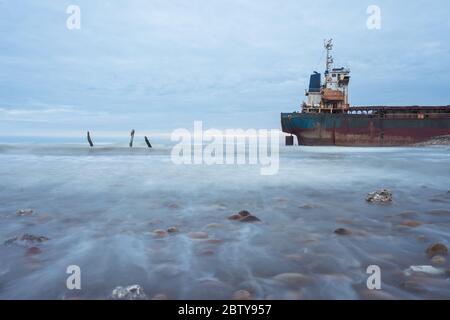 Hsinchu / Taiwan - 15. September 2019: Slow Shutter Landschaftsaufnahme eines rostigen Bootes an der felsigen Küste bei Sonnenuntergang Stockfoto