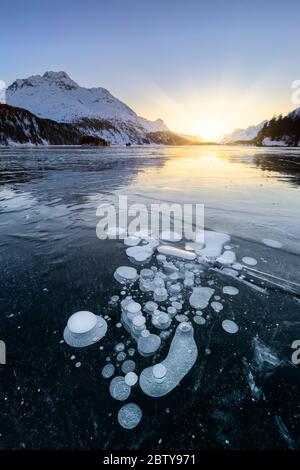 Methanblasen in der eisigen Oberfläche des Silsersees mit schneebedecktem Gipfel, beleuchtet von Sonnenuntergang Licht, Sils See, Engadiner Tal, Kanton Graubünden, Schweiz Stockfoto