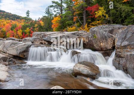 Wasserfall entlang eines Gebirgsflusses an einem bewölkten Herbstmorgen. Atemberaubende Herbstfarben im Hintergrund. Stockfoto