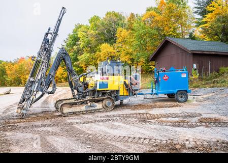 Schwere Erdbohrmaschine auf einer Baustelle mit Bäumen im Hintergrund an einem bewölkten Herbsttag Stockfoto