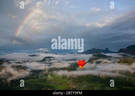 Ein Sonnenaufgang über Vang Vieng, mit einem Regenbogen über den Wolken, als ein Heißluftballon im Vordergrund aufsteigt, Laos, Indochina, Südostasien, Asien Stockfoto