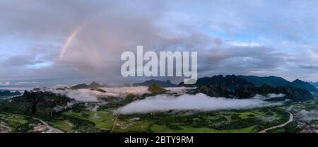 Ein Panorama eines Regenbogens während der Morgenröte über den Bergen von Vang Vieng, Laos, Indochina, Südostasien, Asien bricht Stockfoto