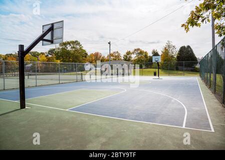 Blick auf einen verlassenen eingezäunten Basketballplatz in einem öffentlichen Park an einem sonnigen Herbstmorgen Stockfoto