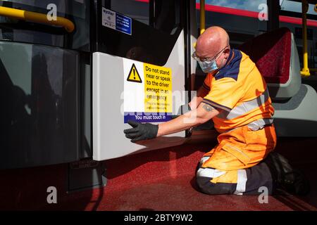 Busmitarbeiter installieren Aufkleber auf einem Bus in der Twickenham Busgarage, um Kunden daran zu erinnern, dass die Fahrpreise auf der Strecke während der COVID-19 pandemi in Betrieb sind Stockfoto