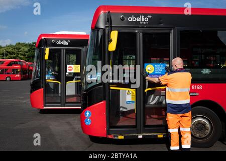 Busmitarbeiter installieren Aufkleber auf einem Bus in der Twickenham Busgarage, um Kunden daran zu erinnern, dass die Fahrpreise auf der Strecke während der COVID-19 pandemi in Betrieb sind Stockfoto