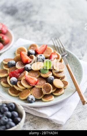Zum Frühstück gab es winzige Pfannkuchen. Cereal Pancakes mit Heidelbeeren, Erdbeeren auf Teller auf grauem Hintergrund. Trendiges Essen. Selektiver Fokus Stockfoto