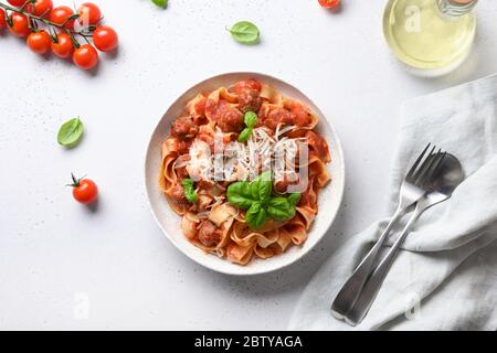 Pasta Fettuccine mit Fleischbällchen, Parmesan, Kirschtomaten, Basilikum auf weißem Tisch. Blick von oben. Stockfoto