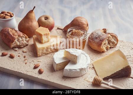 Steinplatte mit verschiedenen Käsesorten im Hintergrund aus weißem Holz Stockfoto