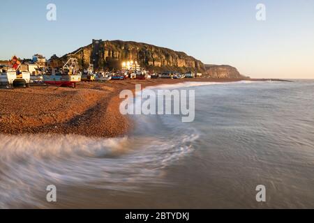 Fischerboote am Strand von Stade mit brechenden Wellen und East Hill hinter bei Sonnenaufgang, Hastings, East Sussex, England, Großbritannien, Europa Stockfoto