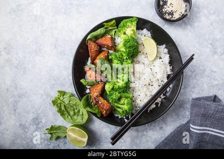 Vegane Teryaki Tempeh oder tempe buddha Schüssel mit Reis, gedämpftem Brokkoli, Spinat und Limette auf grauem Hintergrund. Gesunde Ernährung Stockfoto