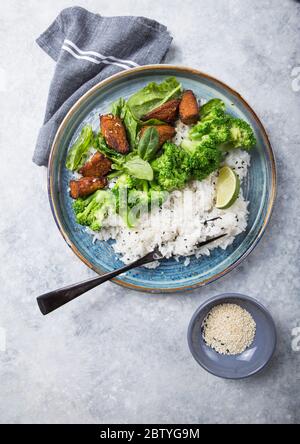 Vegane Teryaki Tempeh oder tempe buddha Schalen mit Reis, gedämpftem Brokkoli, Spinat und Limette auf schwarzem Hintergrund. Gesunde Ernährung Stockfoto