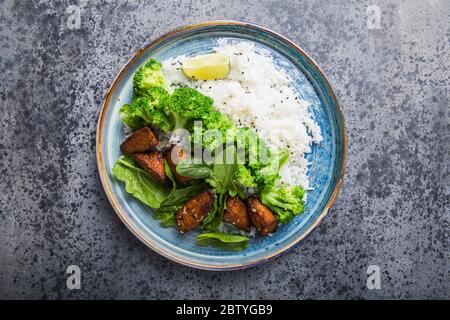 Vegane Teryaki Tempeh oder tempe buddha Schüssel mit Reis, gedämpftem Brokkoli, Spinat und Limette auf grauem Hintergrund. Gesunde Ernährung Stockfoto