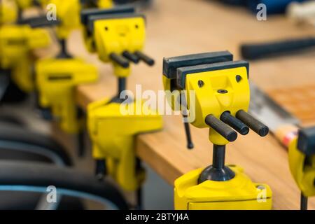 Viele Gelbe Visen sind auf der Arbeitsbank der Schule. Neue Griffe oder Klauen Laster repariert bei Holzbearbeitung Werkstatt. Stockfoto