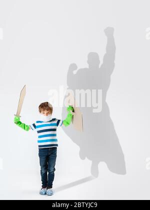 Superheld im Schatten der gewöhnlichen Menschen - moderne Superhelden Konzept, Respekt und Bewunderung. Junge mit Schwert kämpfen mit Coronavirus wie Krieger, die gutes Beispiel. Andere inspirieren. Stockfoto