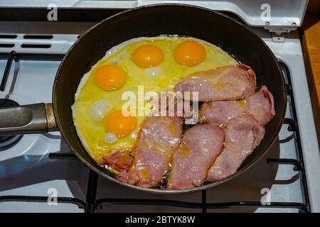 Englisches Frühstück, eine Bratpfanne auf Gasherd mit Speck und Eiern, die gebraten wurden Stockfoto