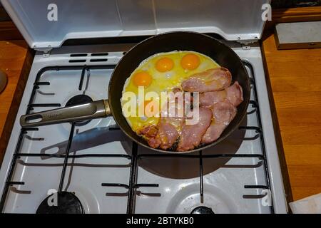 Englisches Frühstück, eine Bratpfanne auf Gasherd mit Speck und Eiern, die gebraten wurden Stockfoto