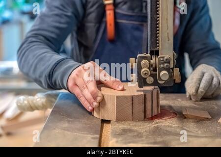 Der Zimmermann schneidet das Holzstück mit der Ausrüstung auf dem Stand. Die Hand des Mannes macht ein rundes Detail aus dem Log. Tischler verwendet elektrische Säge t Stockfoto