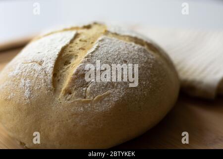 Ein Laib hausgemachter Sauerteig Hefe Brotscheibe mit einer einfachen Cross-Style-Scoring-Technik auf einem Holzbrett. Dunkler und stimmungsvolles Design. Stockfoto