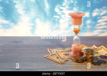 Zeit ist Geld. Finanzkonzept des Geldes mit einer Uhr und Münzen verschiedener Länder. Sanduhr. Stockfoto