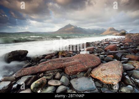 Wellen schlagen gegen Felsen und Kieselsteine in der Elgol Bay vor der atemberaubenden Kulisse der Black Cullins. Highlands, Isle of Skye, Schottland Stockfoto