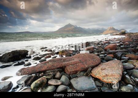 Wellen schlagen gegen Felsen und Kieselsteine in der Elgol Bay vor der atemberaubenden Kulisse der Black Cullins. Highlands, Isle of Skye, Schottland Stockfoto