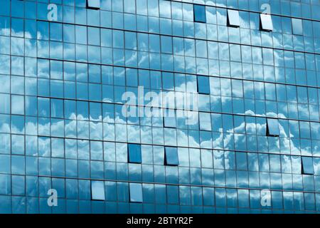 Blauer Himmel und Wolken Reflexionen oder Reflexionen an moderner Büroblauer Glasfassade als symmetrisches Architekturkonzept Stockfoto