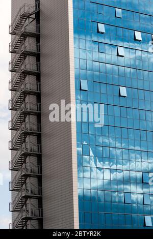 Feuertreppe in Bürogebäuden und Reflektionen von blauem Himmel und Wolken auf der blauen Glasfassade Stockfoto