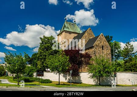 Kyje, Prag / Tschechische Republik - Mai 27 2020: Blick auf die Kirche des Heiligen Bartholomäus aus Stein hinter einer Mauer. Grüne Bäume, sonniger Tag. Stockfoto