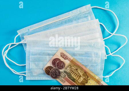 Drei medizinische Masken und russisches Geld, Banknote von 100 Rubel und Münzen auf blauem Hintergrund. Konzept des Wachstumspreises der Gesichtsmaske. Draufsicht Stockfoto