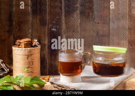 Heilgetränk aus Birkenpilz Chaga, Pilzstücke, Zweig auf Holzplanke auf alter Holzkulisse. Chaga Kaffee oder Tee. Starke antioxidative Impr Stockfoto