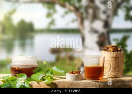 Heiltee aus Birkenpilz Chaga und Chaga Pilz Stücke auf verschwommenen Hintergrund der Birke Baum in der Nähe des Sees. Chaga Kaffee oder Tee. Starke antioxidative Impr Stockfoto