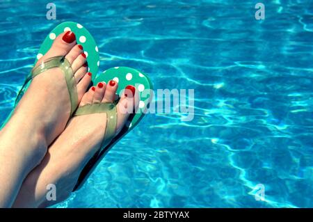 Aqua blau Schwimmbad Rahmen polka-gepunkteten Flip-Flops von einer Frau mit rot bemalten Zehennägel getragen. Stockfoto