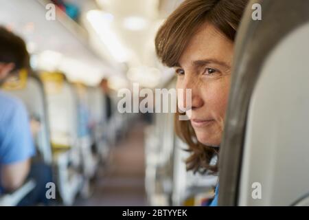 Erwachsene Passagierin, die auf einem bequemen Sitz in der Nähe des Gangs im Flugzeug wegschaut Stockfoto