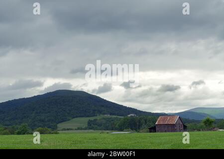 Eine ländliche Szene, die eine alte Scheune auf einer Heuweide mit Sturmwolken über dem Kopf und Bergen im Hintergrund zeigt. Stockfoto