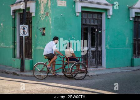 Mann auf dem Fahrrad mit einer Frau, die in einem Wagen vorne in Valladolid, Yucatan, Mexiko sitzt Stockfoto