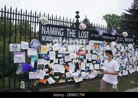 New York, NY, USA. Mai 2020. Ein Mann mit einer Maske geht an einem Denkmal für COVID-19-Opfer vorbei, das während der COVID-19-Pandemie am 28. Mai 2020 in New York an einem Zaun am Eingang zum Green-Wood-Friedhof hängt. Kredit: Bryan Smith/ZUMA Wire/Alamy Live News Stockfoto