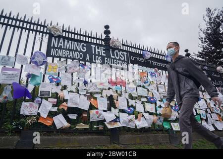 New York, NY, USA. Mai 2020. Ein Mann mit einer Maske geht an einem Denkmal für COVID-19-Opfer vorbei, das während der COVID-19-Pandemie am 28. Mai 2020 in New York an einem Zaun am Eingang zum Green-Wood-Friedhof hängt. Kredit: Bryan Smith/ZUMA Wire/Alamy Live News Stockfoto