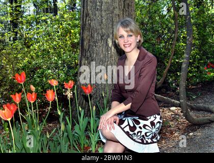 Schöne junge Frau genießt die FrühlingsTulpen im Garvans Woodland Garden in Hot Springs, Arkansas. Sie kniet neben einem Baum und trägt jacke Stockfoto