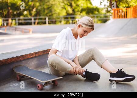 Junge Skater Mädchen hält ihr schmerzhaftes Bein mit Skateboard in der Nähe am Skatepark Stockfoto