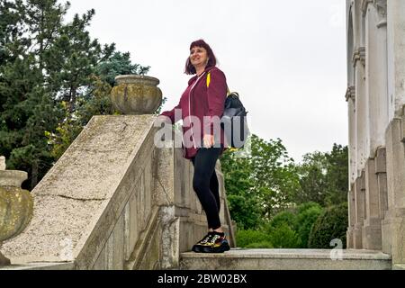 Eine junge, schöne Frau, die glücklich auf einem Balkon im Park posiert. Sie hatte gerade eine positive und freudige Nachricht über das Telefon erhalten. Stockfoto