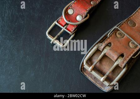 Fragment von zwei alten echten Lederhalsbändern auf einem dunklen Tisch. Zerbrochene, schäbige Leder- und Metallbeschläge. Echte Vintage Hundehalsbänder. Liebe zu den Tieren. Stockfoto